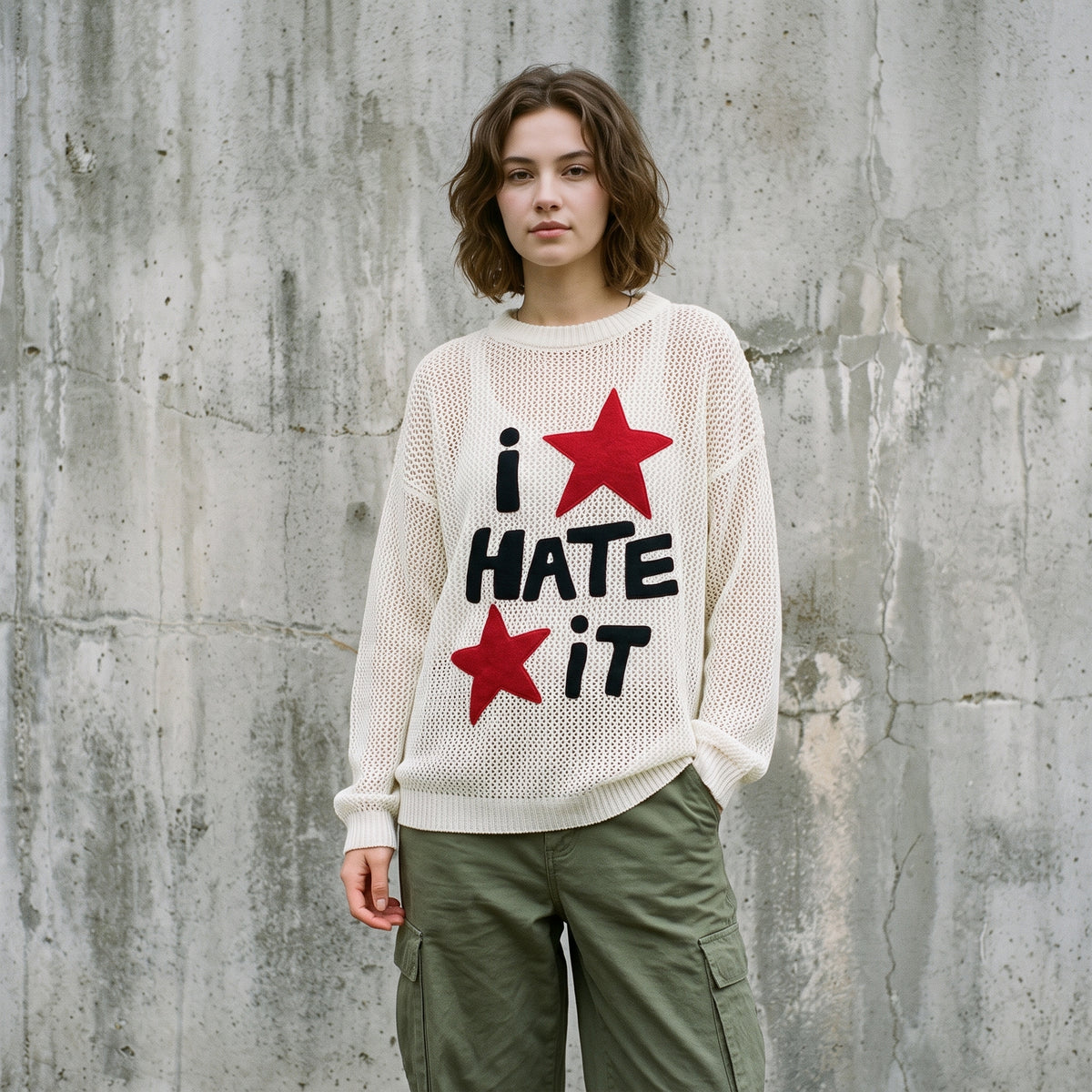 Woman wearing the cream open-knit I Hate It sweater with red star appliques