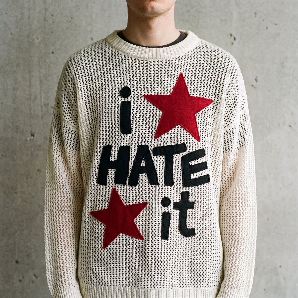 Close-up of the i HATE iT slogan and red stars on the cream knit sweater