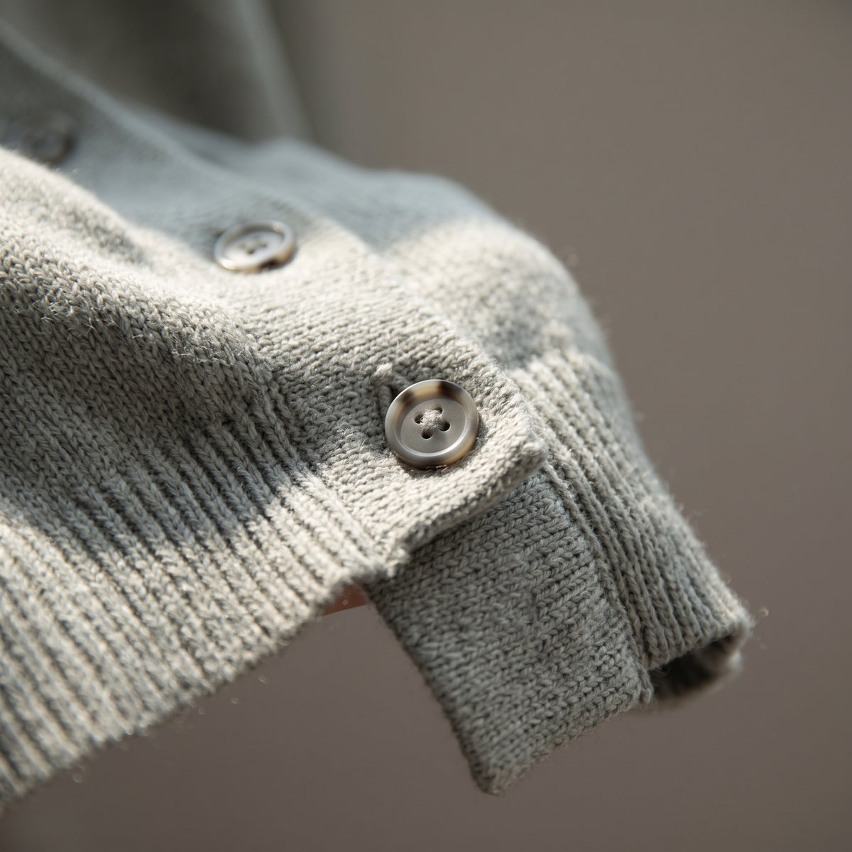 Detail of the fine knit, button and ribbed hem of the sage cardigan