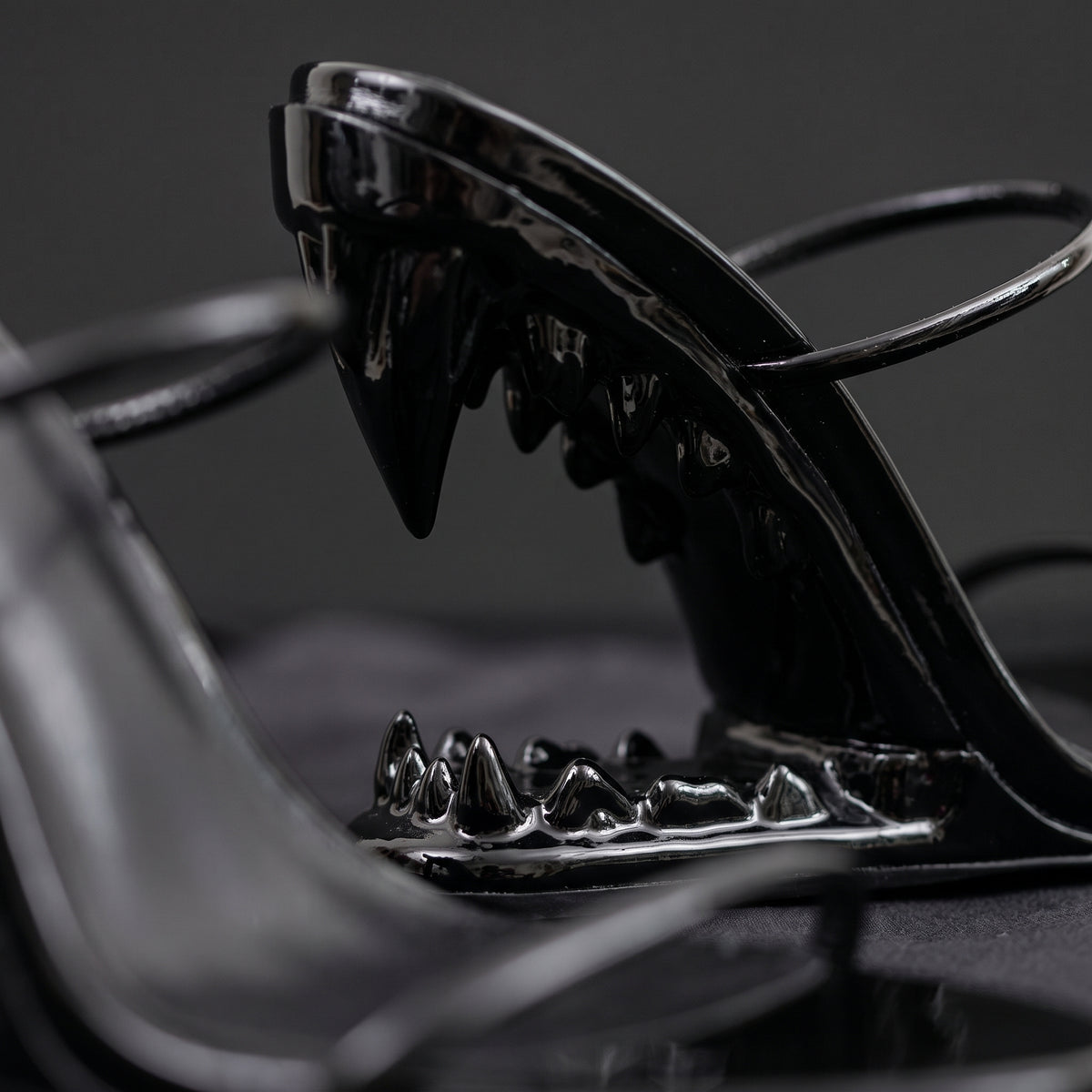 Macro detail of the sculpted open-jaw teeth heel in glossy black patent